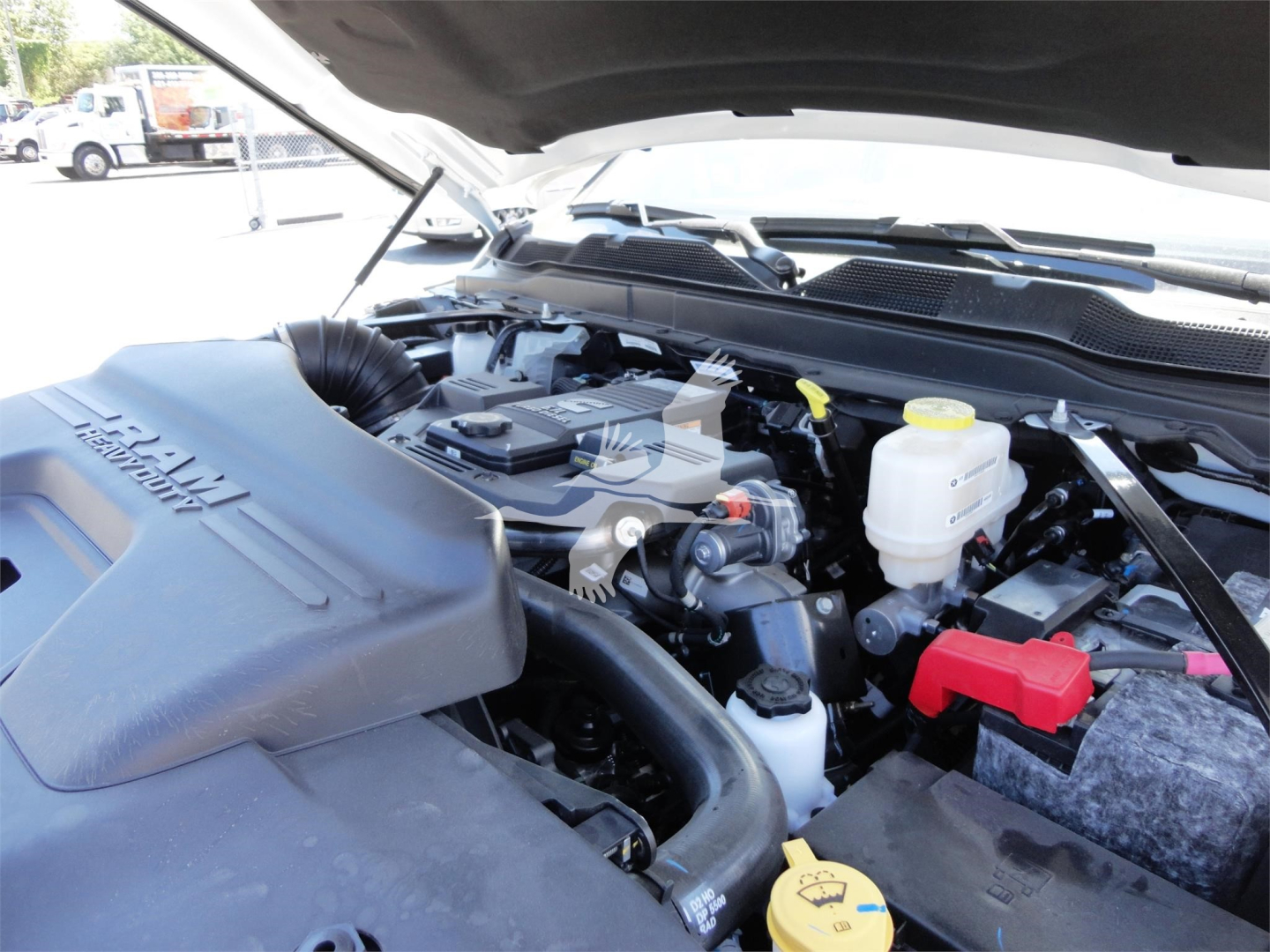 Ram 5500 HD engine bay showing coolant reservoir, yellow dipstick, power steering area, and red 12V battery terminal cover under open hood.