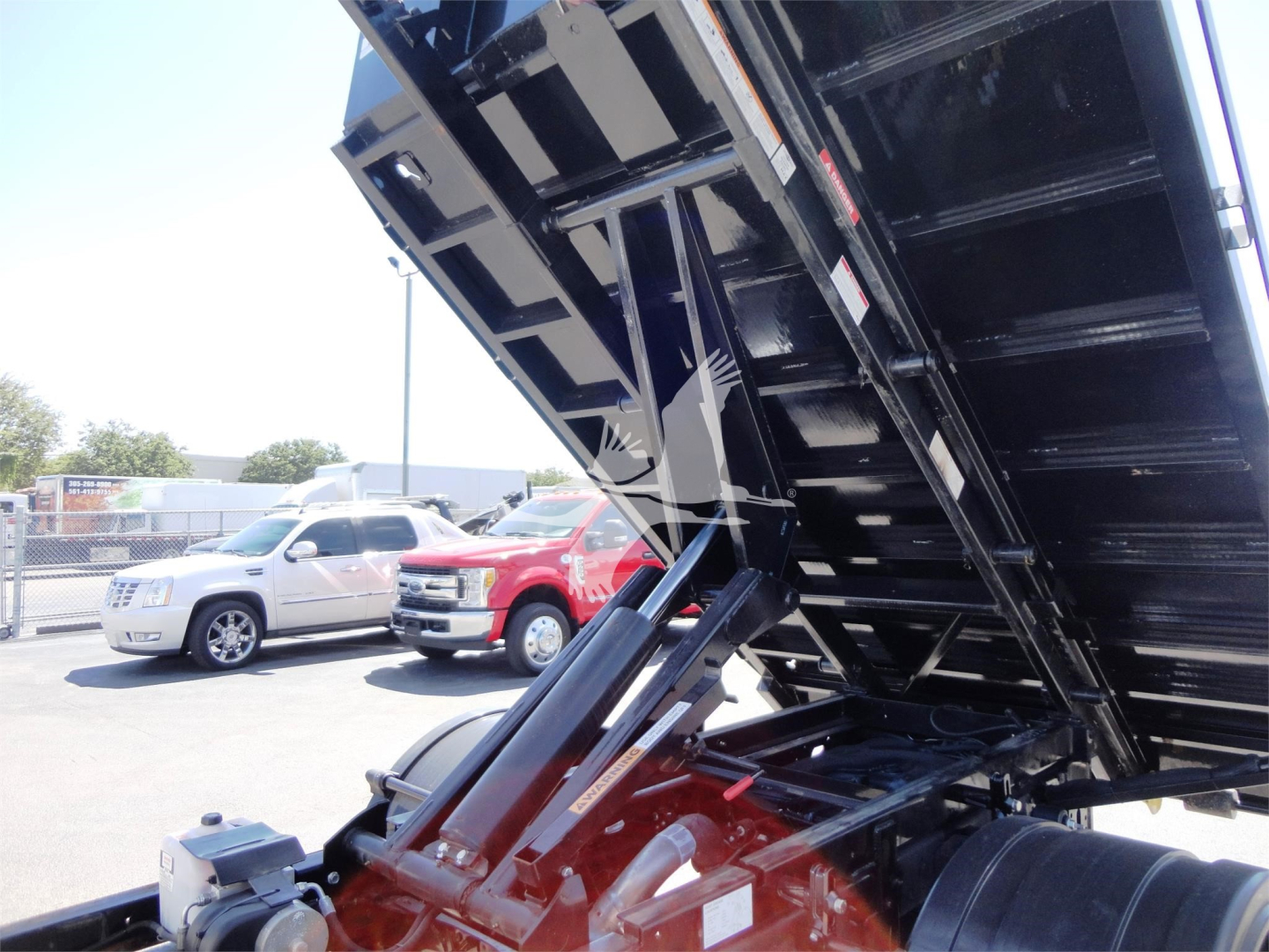 Ram 5500 HD truck with a lifted hooklift bed showing hydraulic lifting mechanism and metal bed in upraised position.