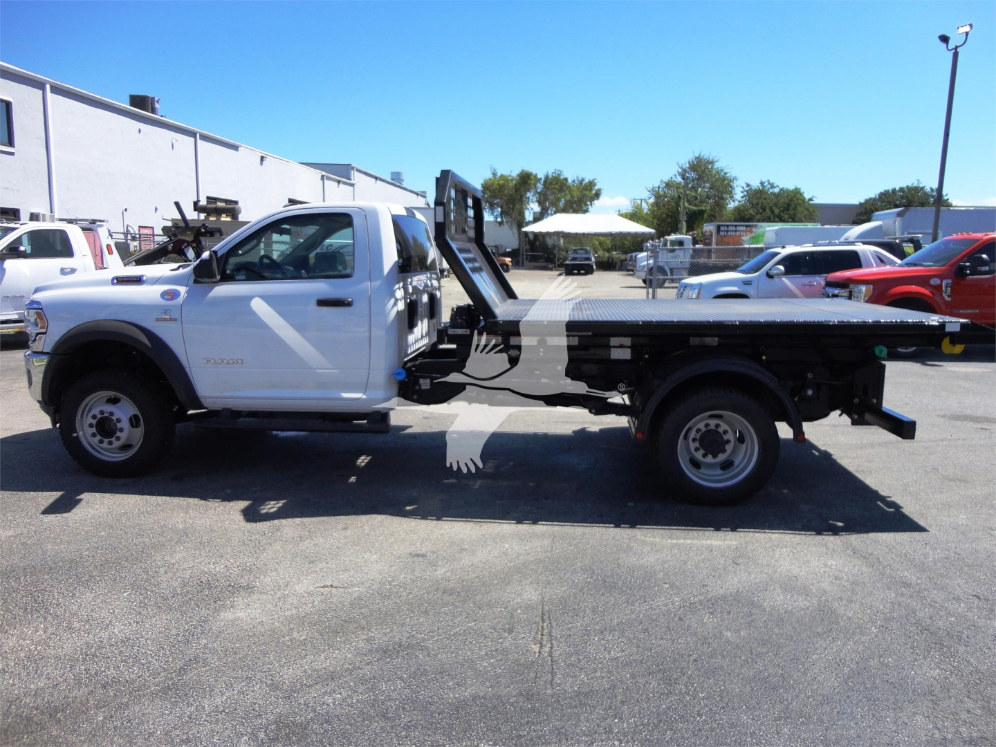 Truck side view showing a white Ram 5500 HD with a hooklift bed and elevated hydraulic winch/ram assembly.