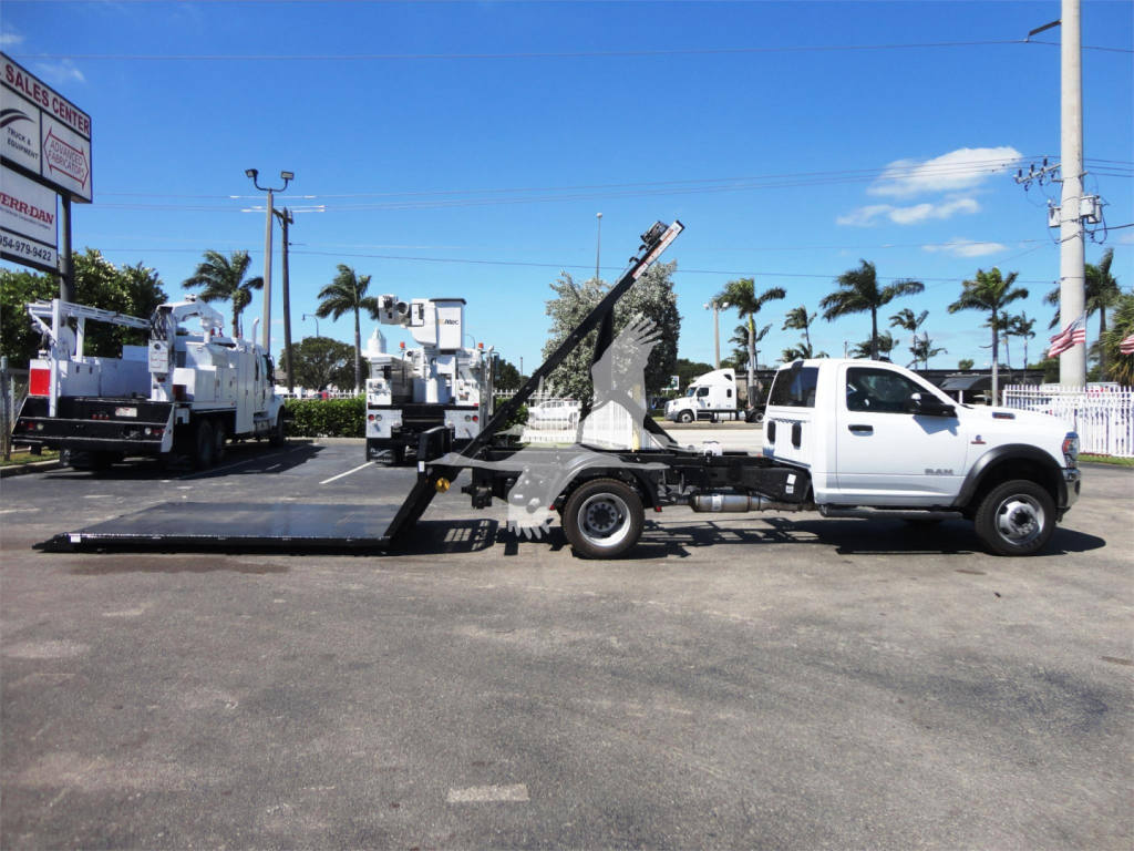 Ram 5500 dual-wheel trucks with a long black hooklift bed and a white cab, side profile view, dealership lot in the background.