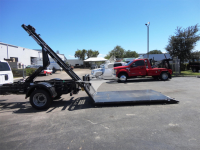 Ram 5500 HD hooklift truck with a flatbed and hydraulic loading ramp in a dealership lot.