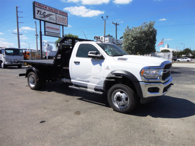 RAM 5500 HD truck with flatbed/telescopic hoist and black steel bed; white cab; side view showing 'RAM 5500' badge and dual rear wheels; yard with dealership signs in background.