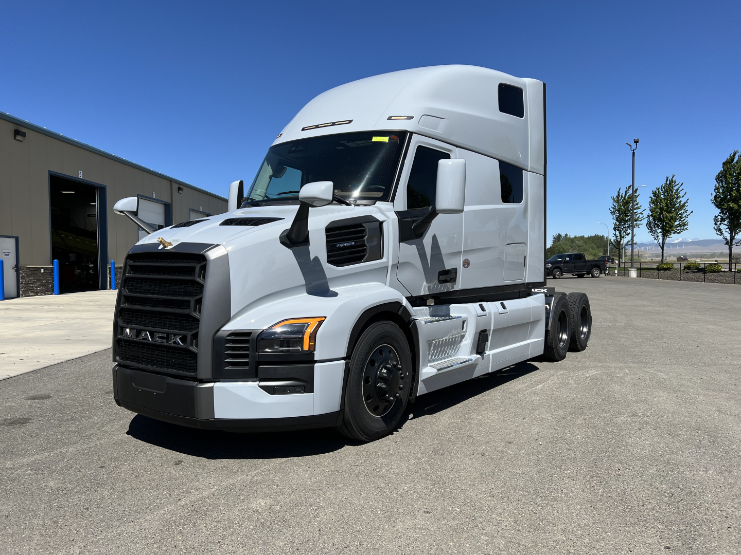 Mack PR64T76H tractor-trailer cab in light gray, side view, with dual rear axles, front grille and headlights.