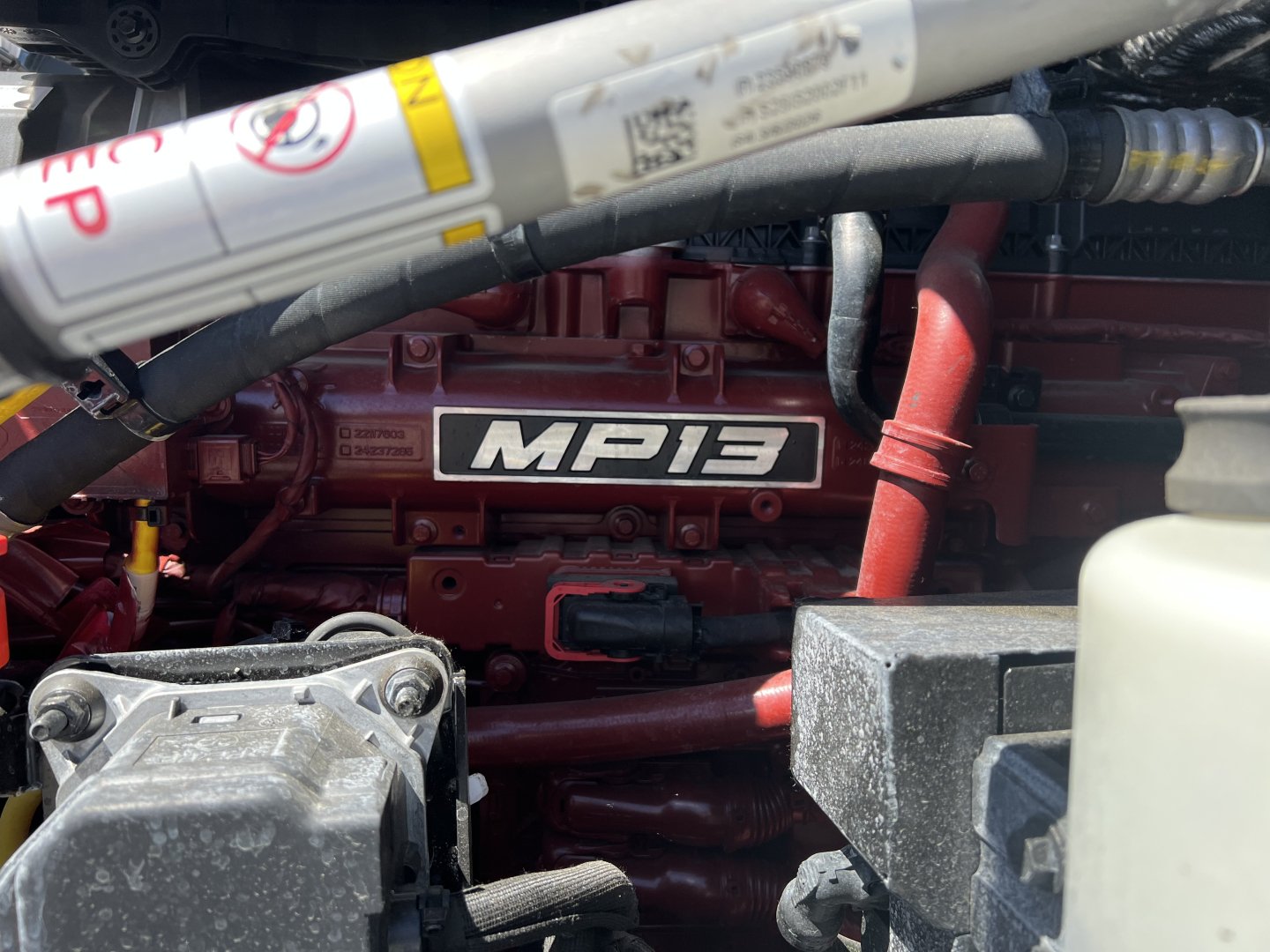 Engine bay of a 2027 Mack PR64T76H showing the MP13 engine cover and surrounding hoses and components.