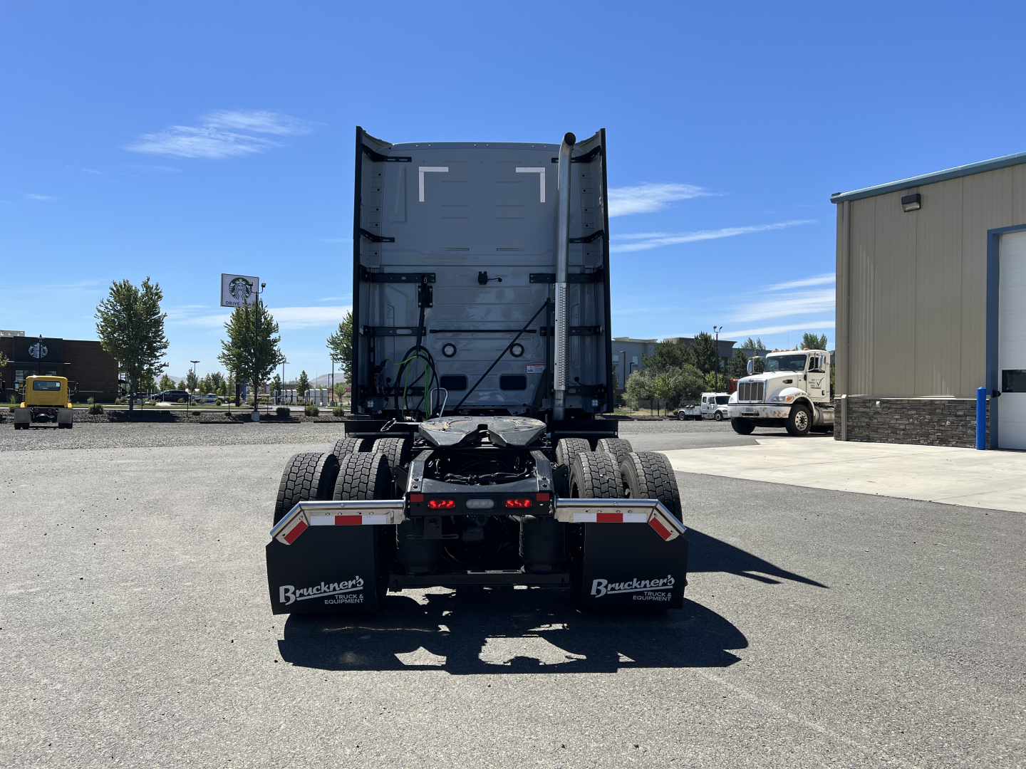 Rear view of a Mack tractor chassis showing the fifth wheel and mud flaps with Mack branding and Brackner? dealer logo. No visible engine or labels readable.