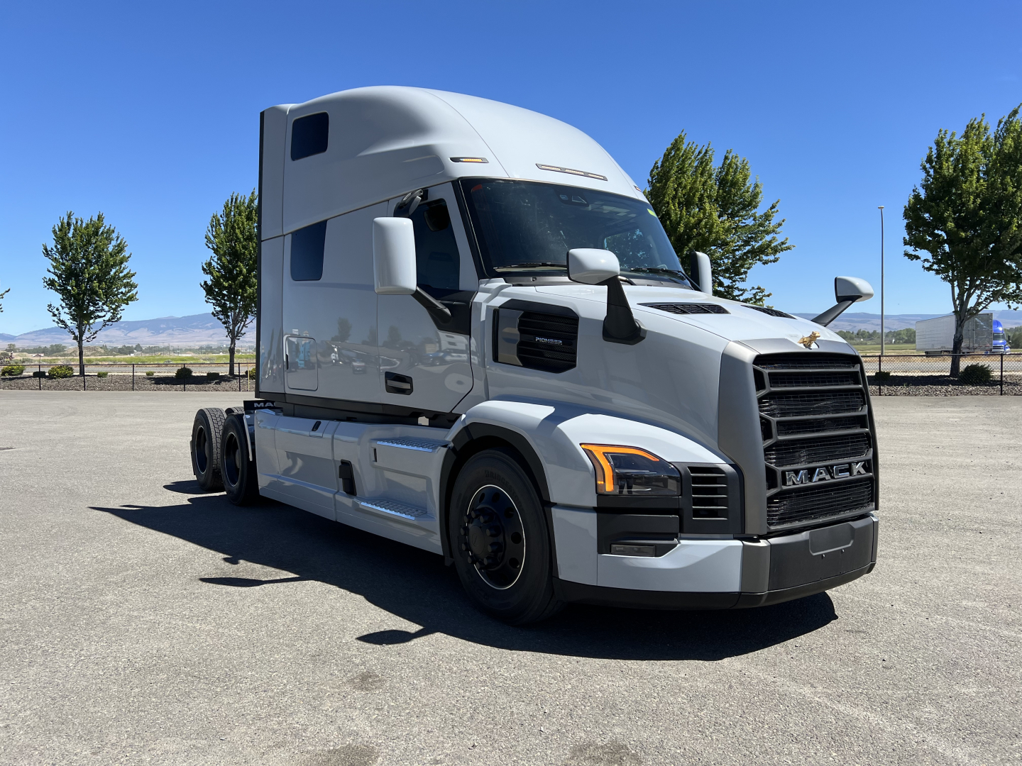 Mack PR64T76H tractor-trailer cab in a parking lot, front-right view, with silver paint and large grille.