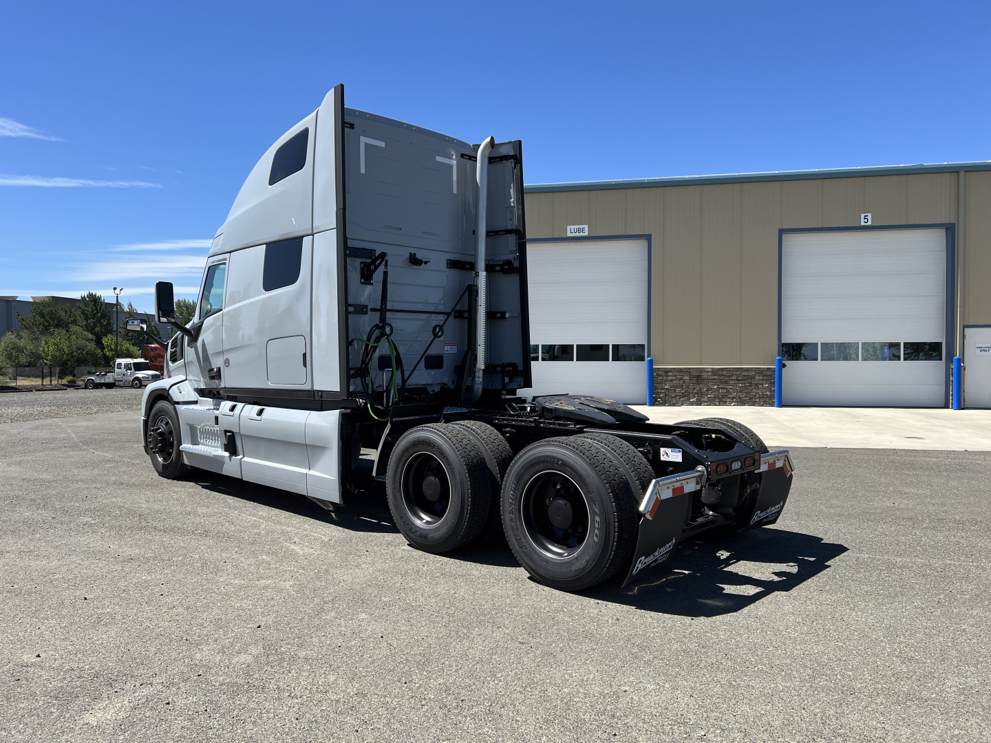 Truck cab and rear chassis of a new Mack PR64T76H tractor, side view showing sleeper cab and dual rear axles.