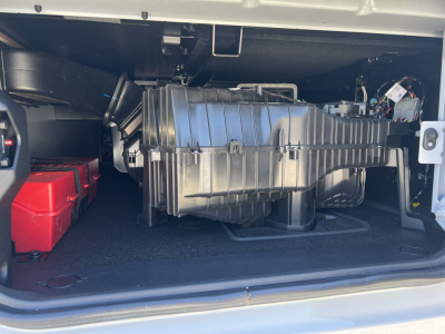 Truck engine compartment showing large air intake/plenum and wiring harness in side compartment; red battery box visible on left.