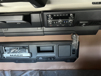 Cab interior of a Mack PR64T76H truck dashboard showing control panel and storage compartments.