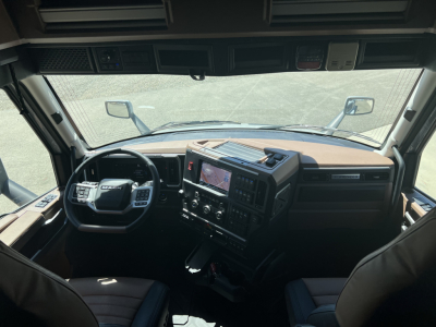 Cab interior of a Mack truck PR64T76H showing steering wheel, dashboard with large touchscreen, center console, side mirrors, and windshield from driver’s perspective.