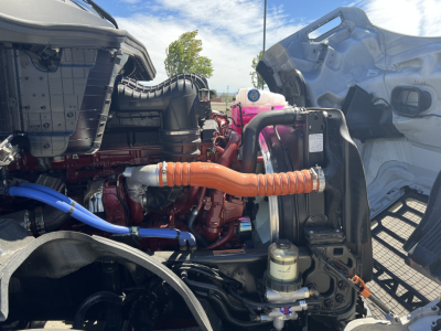Truck engine bay with orange coolant hose and pink coolant reservoir; blue hoses and black components visible; radiator and intake area in view.