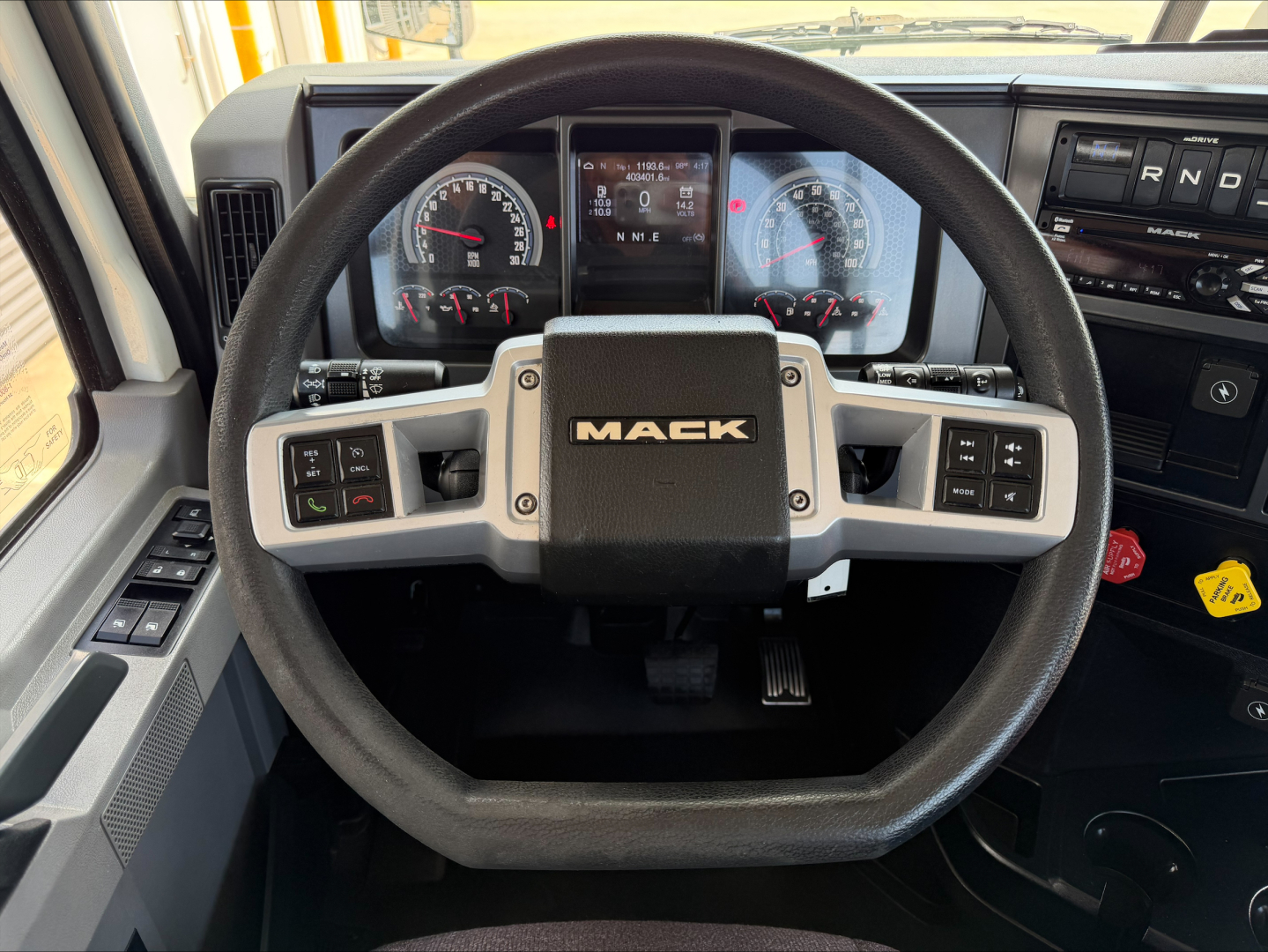 Steering wheel with Mack logo and instrument cluster visible in truck cab; dashboard controls and gear selector visible on right.