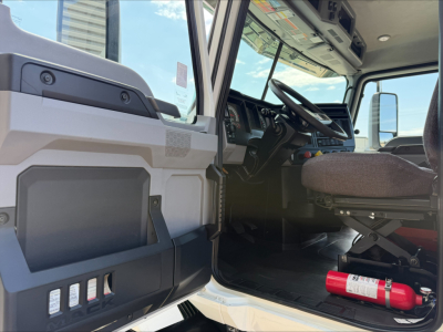 Truck cab interior of a 2020 Mack Anthem, front door open, showing steering wheel, dashboard, driver's seat, and a red fire extinguisher on the floor.