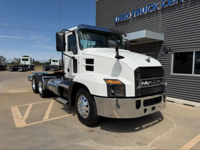 Truck front three-quarter view showing a white Mack Anthem cab at a used truck lot, with chrome bumper and black grille; visible text includes MACK on grille and surrounding dealership building