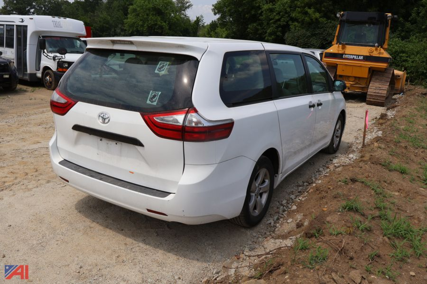 2017 Toyota Sienna minivan rear view showing tail lights and back hatch, white exterior, parked on dirt lot with construction equipment in background.