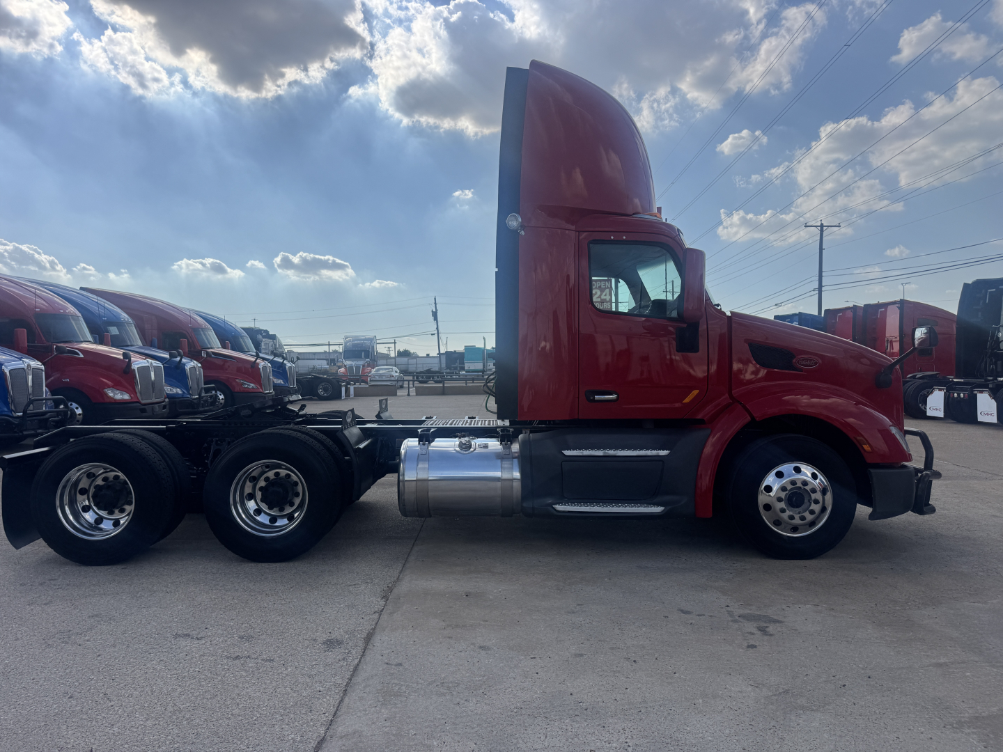 Peterbilt 579 conventional daycab tractor side view showing red cab, fuel tanks, and third wheelset with chrome wheels.