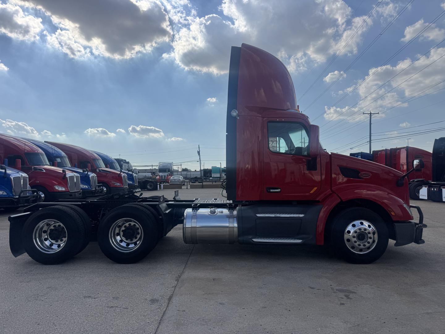 Peterbilt 579 daycab side profile showing red cab and chrome fuel tanks in a truck lot.