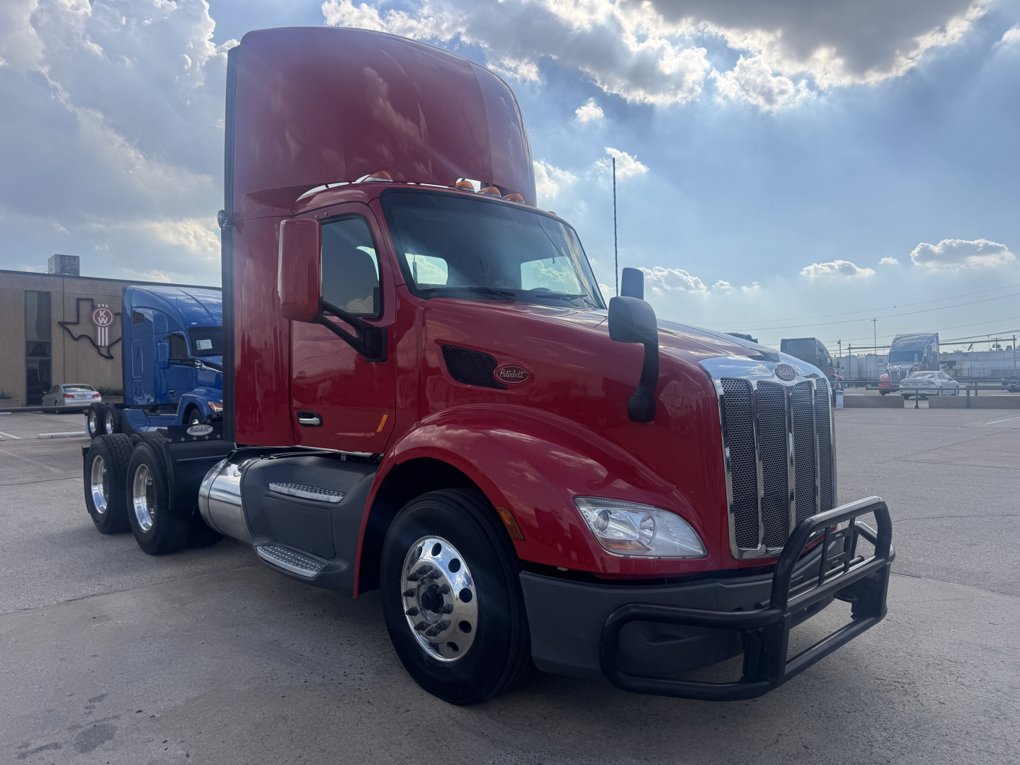 Peterbilt 579 semi-truck in red, front right view with high sleeper cab, bumper guard, chrome exhausts and twin rear axles.