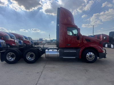 Peterbilt 579 conventional daycab tractor side view showing red cab, fuel tanks, and third wheelset with chrome wheels.