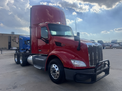 Peterbilt 579 conventional daycab tractor in red, front three-quarter view, showing large chrome grille, dual rear wheels, and high sleeper, parked lot.