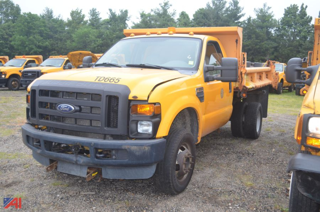 Ford F-350 Super Duty dump truck with plow mounting, yellow cab and dump bed, front grille, headlights, and large side mirrors visible in a row of similar trucks.