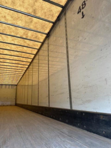 Van trailer interior showing metal side walls and wooden floor with overhead support beams.