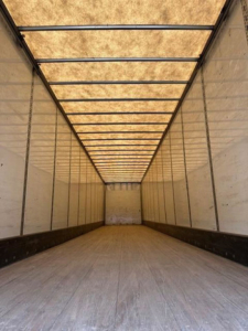 Trailer interior showing long empty cargo space with wooden ceiling panels and side walls; light from translucent roof panels.