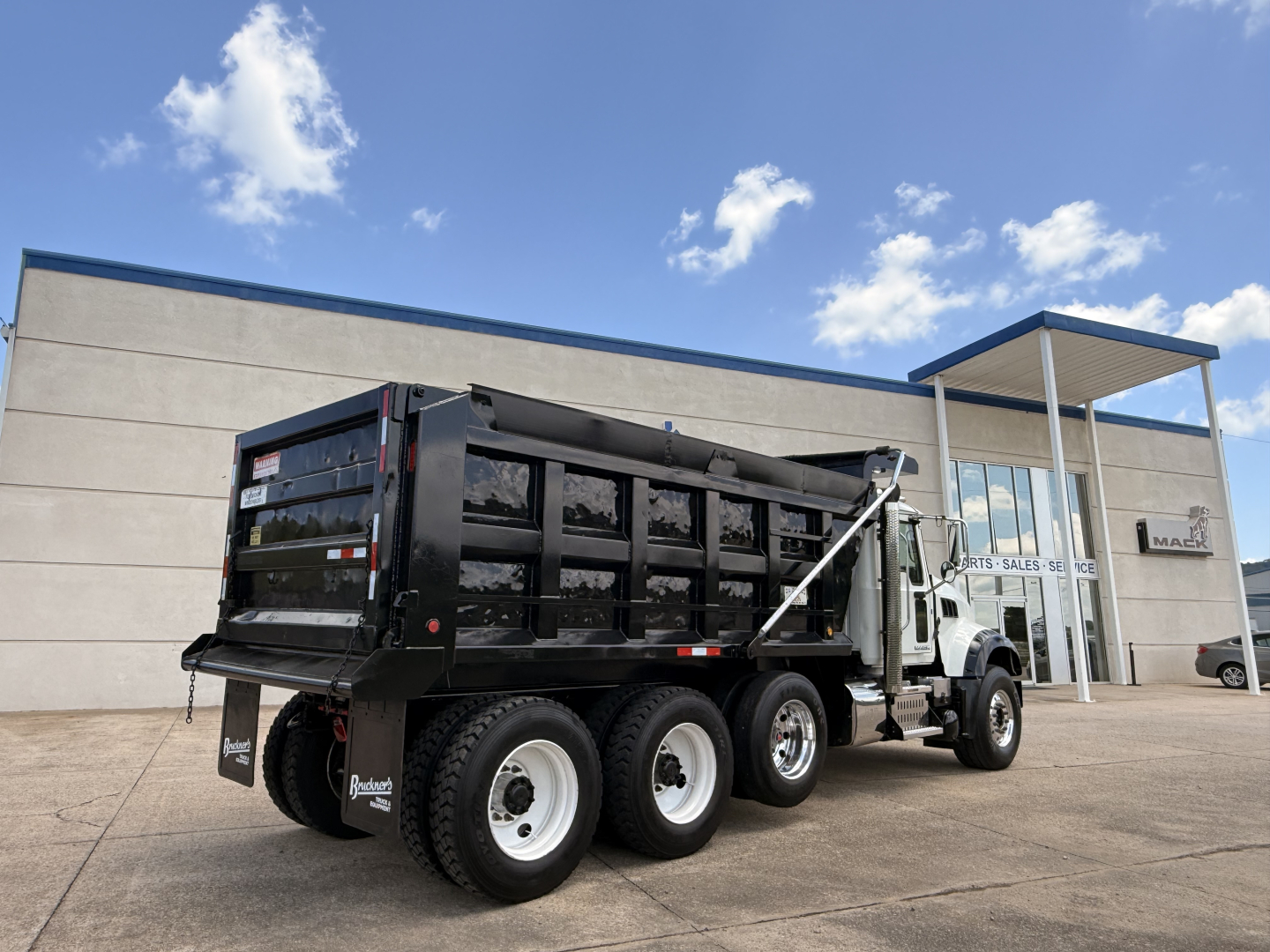 2016 Mack GU713 dump truck with black dump body, white cab, three rear axles, dual rear wheels, VIN plate area not visible, stock number B3739P, dealership building in background.