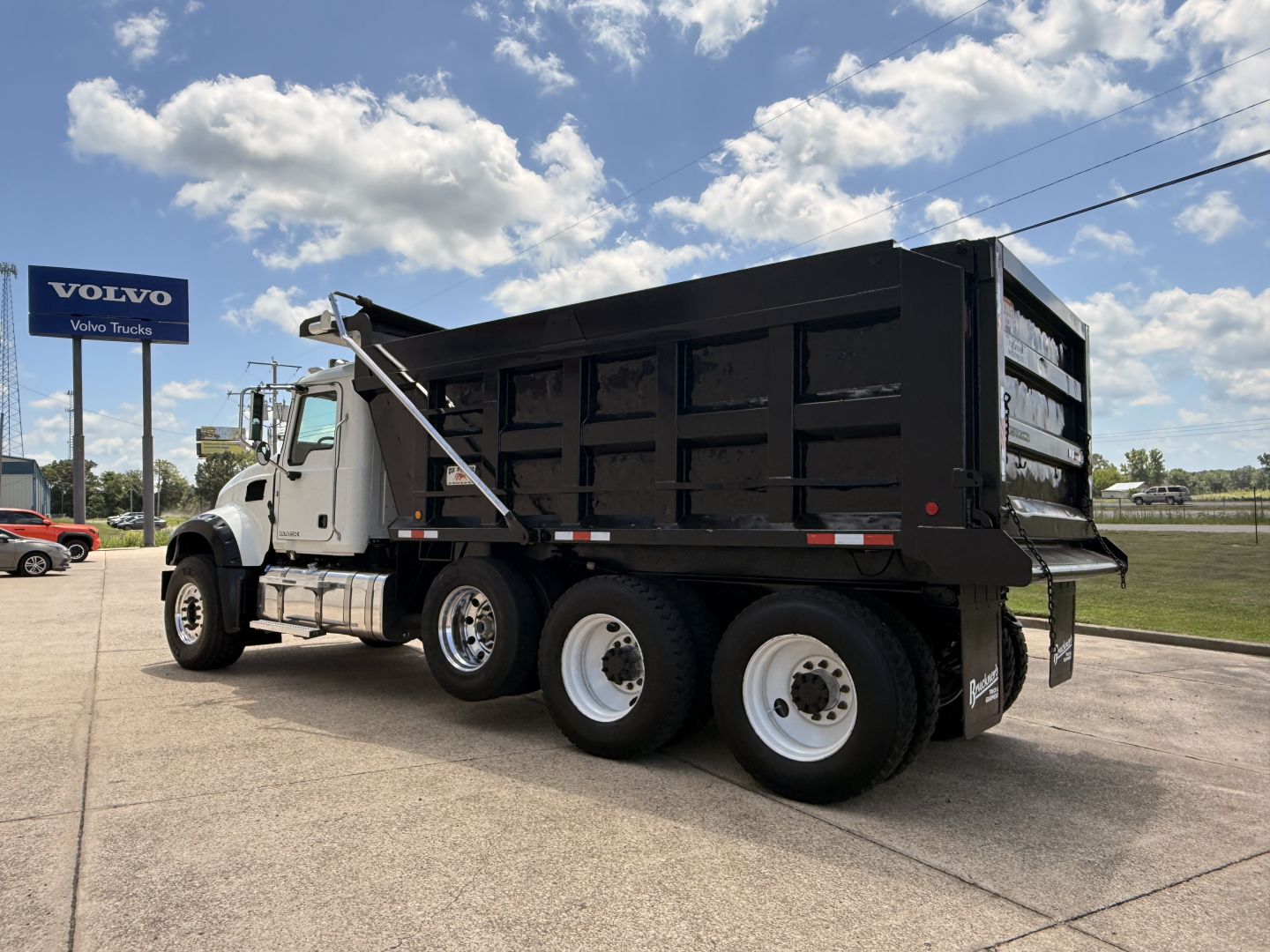 Dump truck chassis and cargo bed of a 2016 Mack GU713 with black dump body, white cab, on dealership lot.