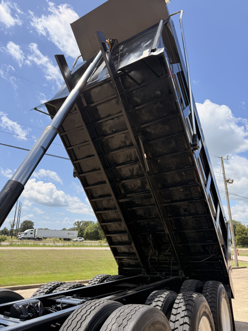 Dump truck bed in raised position with hydraulic cylinder visible, black undercarriage and multiple rear wheels, Mack GU713 likely class 8