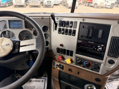 Dashboard and steering wheel area of a Mack GU713 truck showing instrument cluster, steering wheel with Mack logo, various gauges, switch panel, and radio unit.