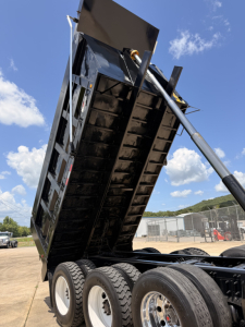 Dump truck bed raised showing hydraulic cylinder and underside of dumping mechanism on a Mack GU713 dump truck. Black steel bed with reinforcement ribs and multiple axles visible.