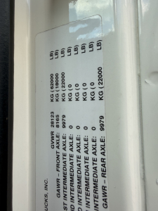 Label plate with drivetrain axle ratings and weights: GAWR - FRONT AXLE, REAR AXLE; kg/lb values and 'GMWR' stamp; multiple columns of 'KG' and 'LB' indicators.