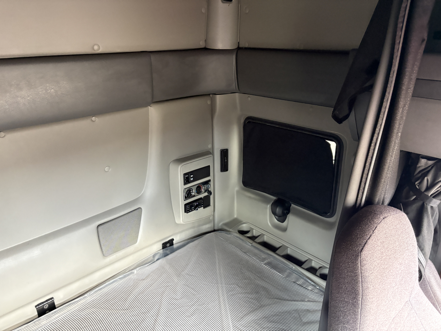 Cab interior of a sleeper truck with light gray wall panels, a small window, and a padded bench/bed area. No legible technical labels visible.