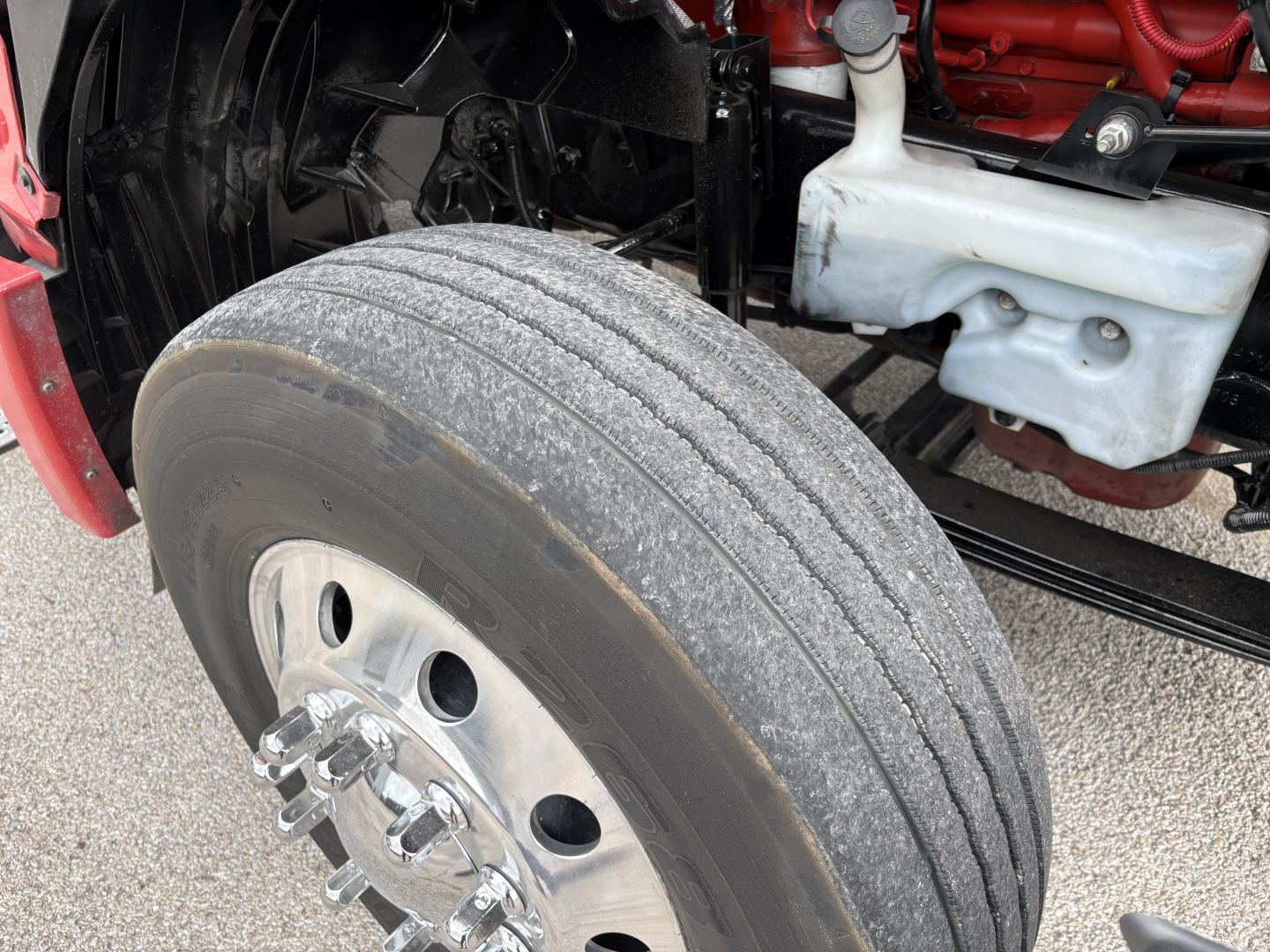 Wheel and front suspension of a 2022 International LT truck showing front dual tires, polished aluminum wheel, part of chassis, coolant reservoir, and engine bay area.