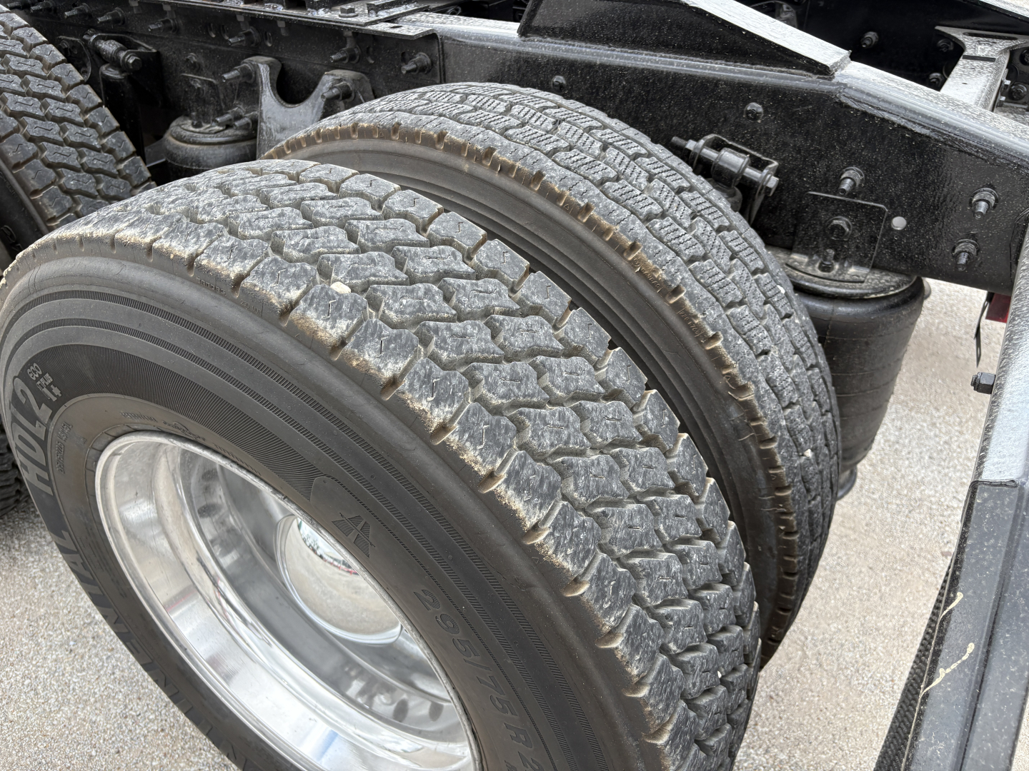 Truck chassis and dual rear wheels showing tire tread and wheel, with frame and suspension components visible.