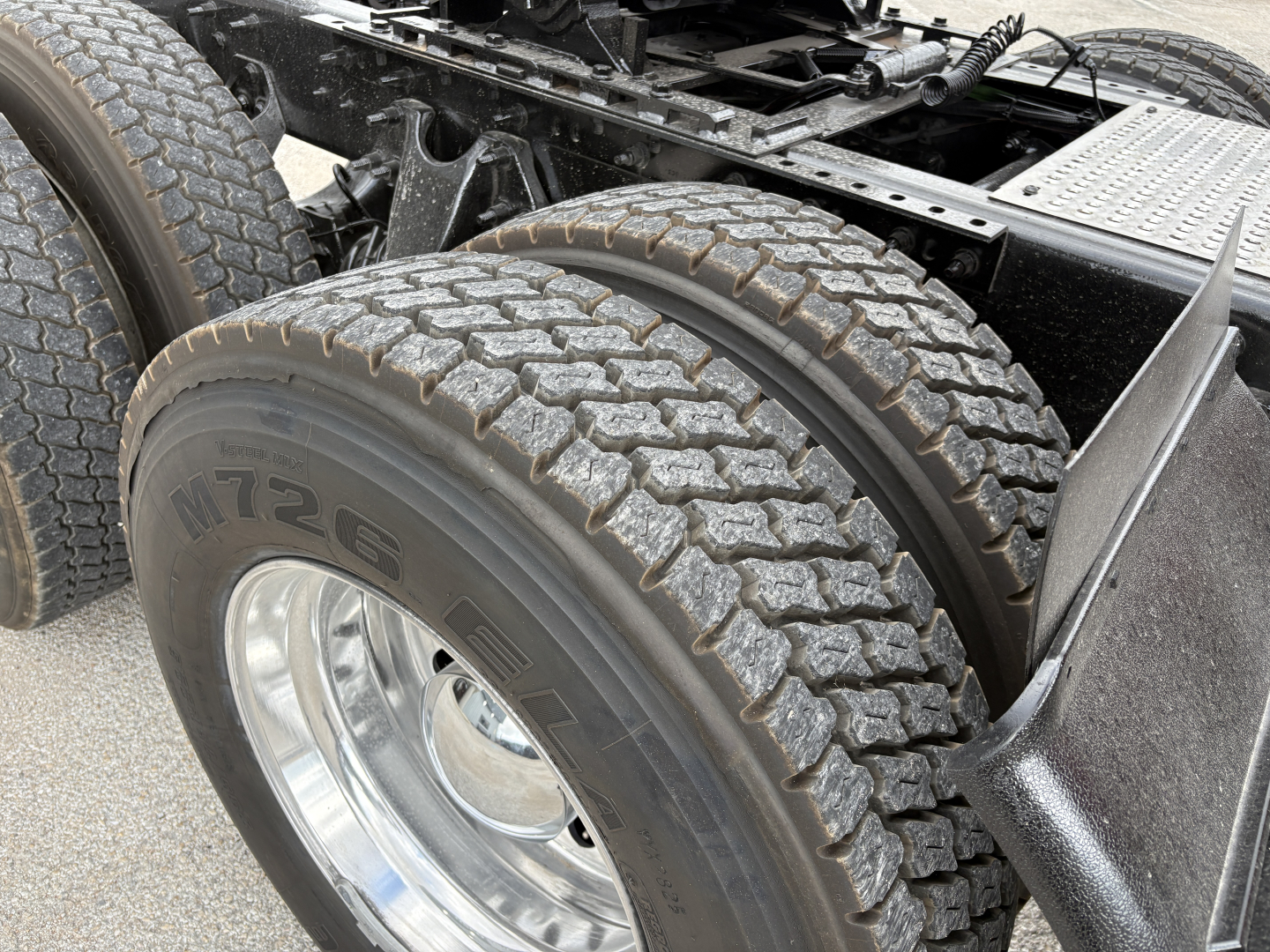 Dual rear tractor tires and chassis of a 2022 International LT truck showing tire treads and fuel/air lines, partial frame and steps.