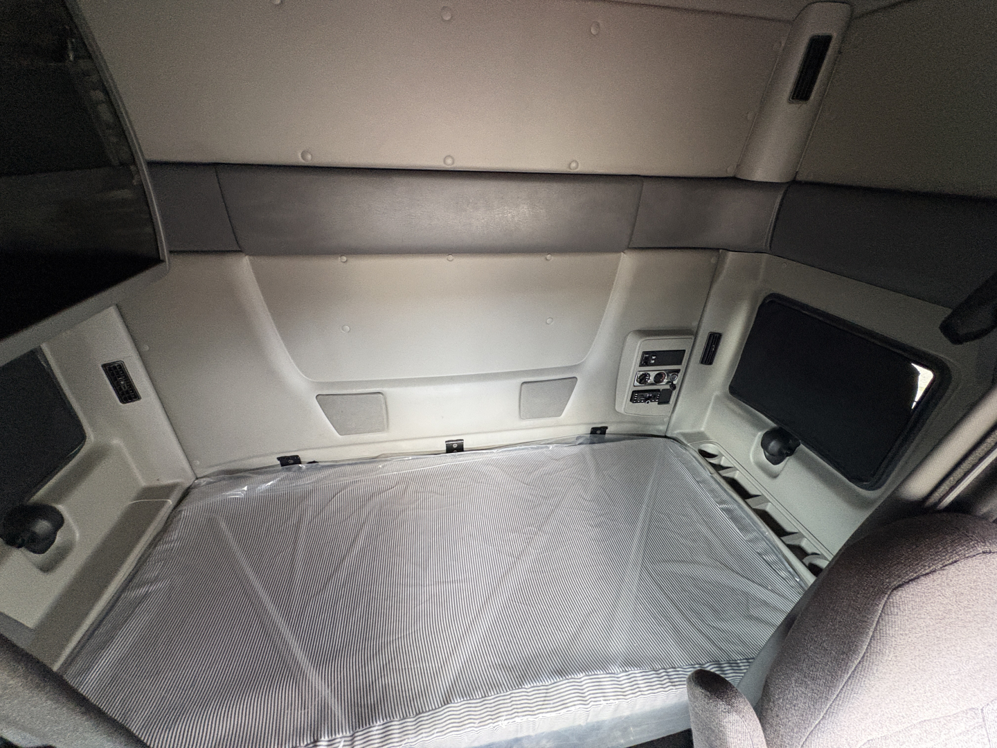 Interior sleeper cab of a 2022 International LT showing a bed with plastic cover, side window, and storage panels.