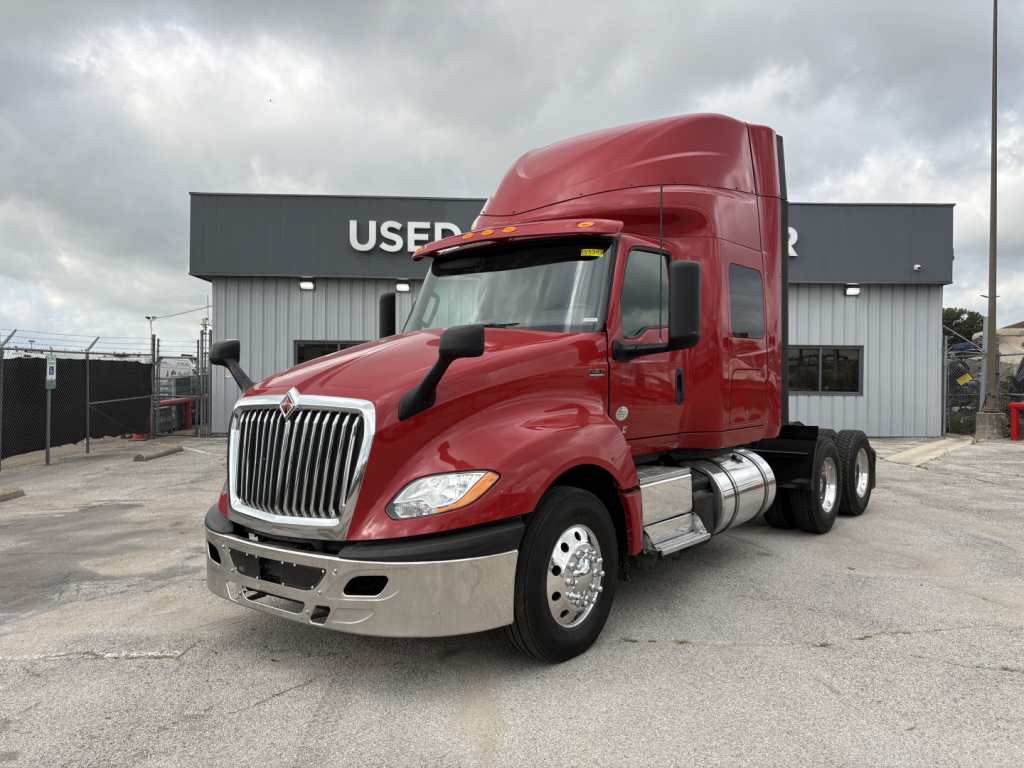 Truck front-left view of a red 2022 International LT sleeper cab semitrailer configuration, showing chrome grille, dual rear axles, and fuel tanks.