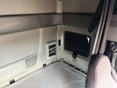 Cab interior of a sleeper truck with light gray wall panels, a small window, and a padded bench/bed area. No legible technical labels visible.