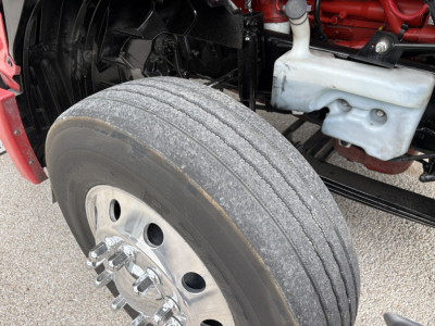 Wheel and front suspension of a 2022 International LT truck showing front dual tires, polished aluminum wheel, part of chassis, coolant reservoir, and engine bay area.