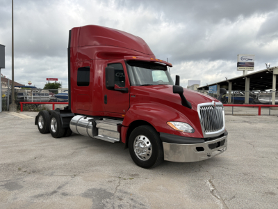 Red International LT semi-truck with sleeper cab, front chrome grille, black mirrors, and chrome fuel tanks. Vehicle sits in a lot with cloudy sky.
