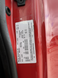 Vehicle data plate on red truck door jamb showing VIN, GVW, axle ratings, and safety information.