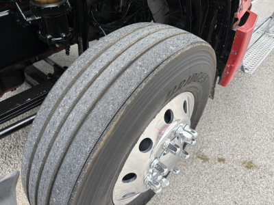 Truck wheel and tire close-up showing tread and chrome lug nuts, part of a 2022 International LT in-spec wheel assembly.
