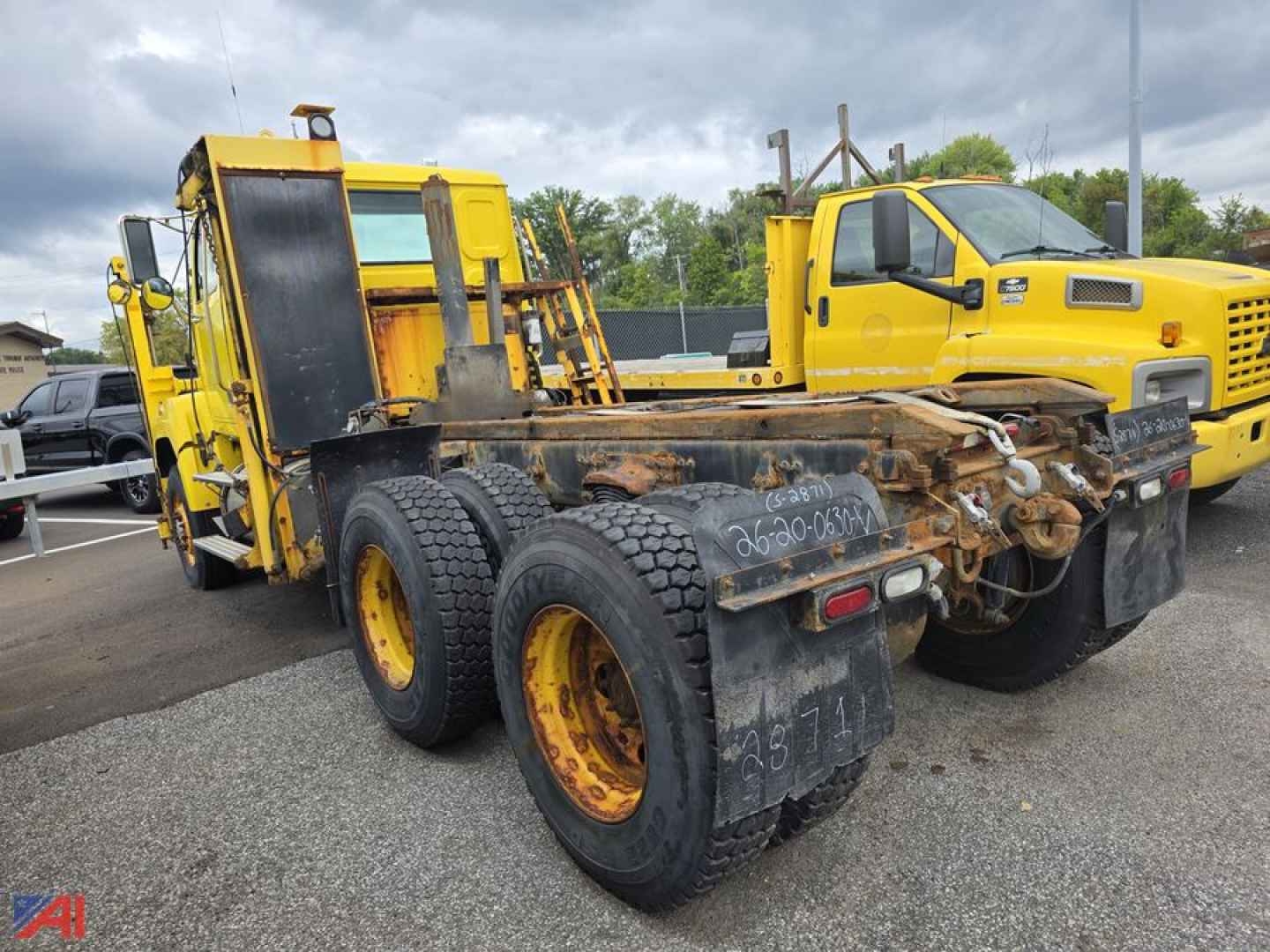 Rear view of a yellow cab and chassis truck with a rusty, heavy-duty dual rear axle and attached trailer coupling, showing worn trailers and wheel rims.