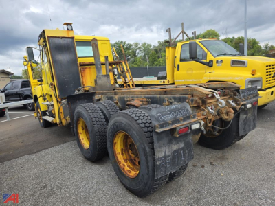 Rear view of a yellow cab and chassis truck with a rusty, heavy-duty dual rear axle and attached trailer coupling, showing worn trailers and wheel rims.