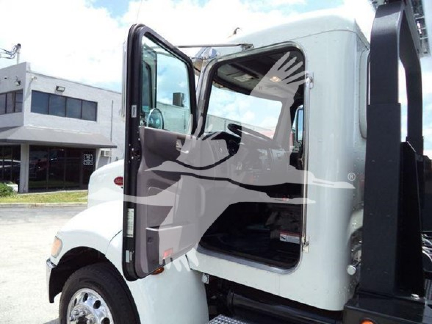 Peterbilt 337 rollback truck cab with open door showing interior, side mirror, and part of hydraulic rollback equipment.