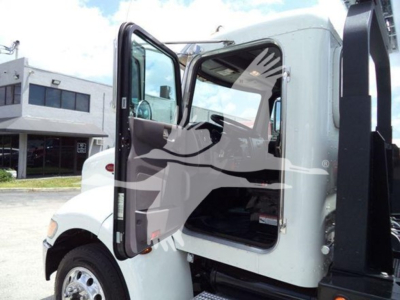 Peterbilt 337 rollback truck cab with open door showing interior, side mirror, and part of hydraulic rollback equipment.