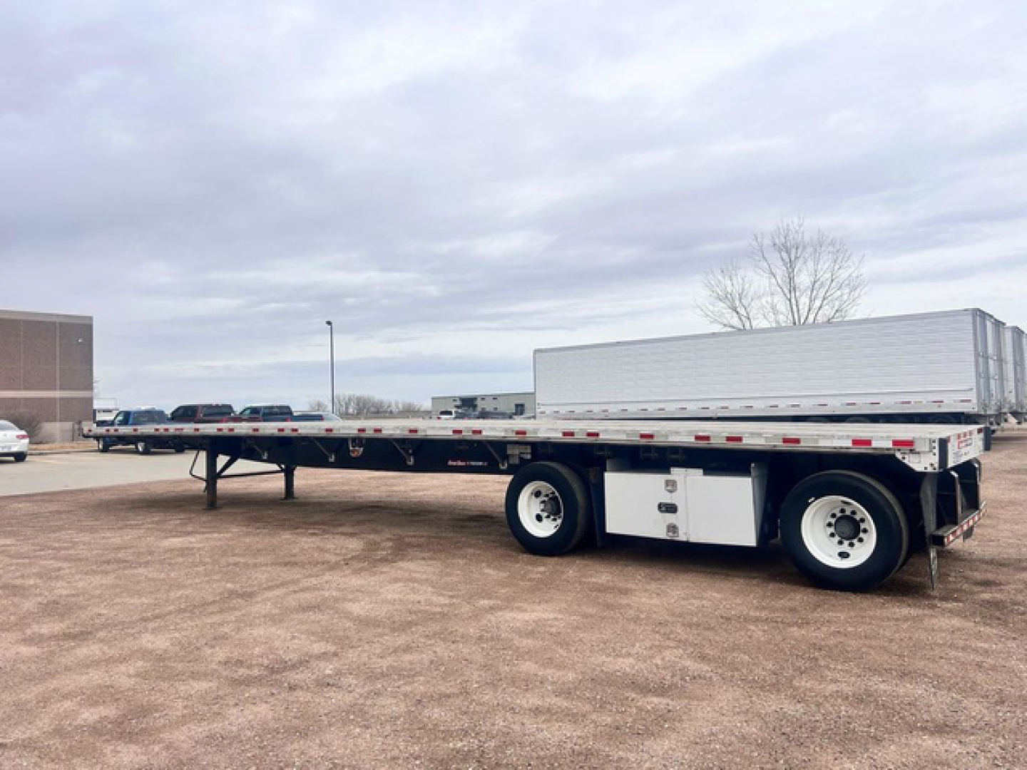 Flatbed trailer with long steel deck and dual rear axles, Great Dane trailer in a gravel lot.