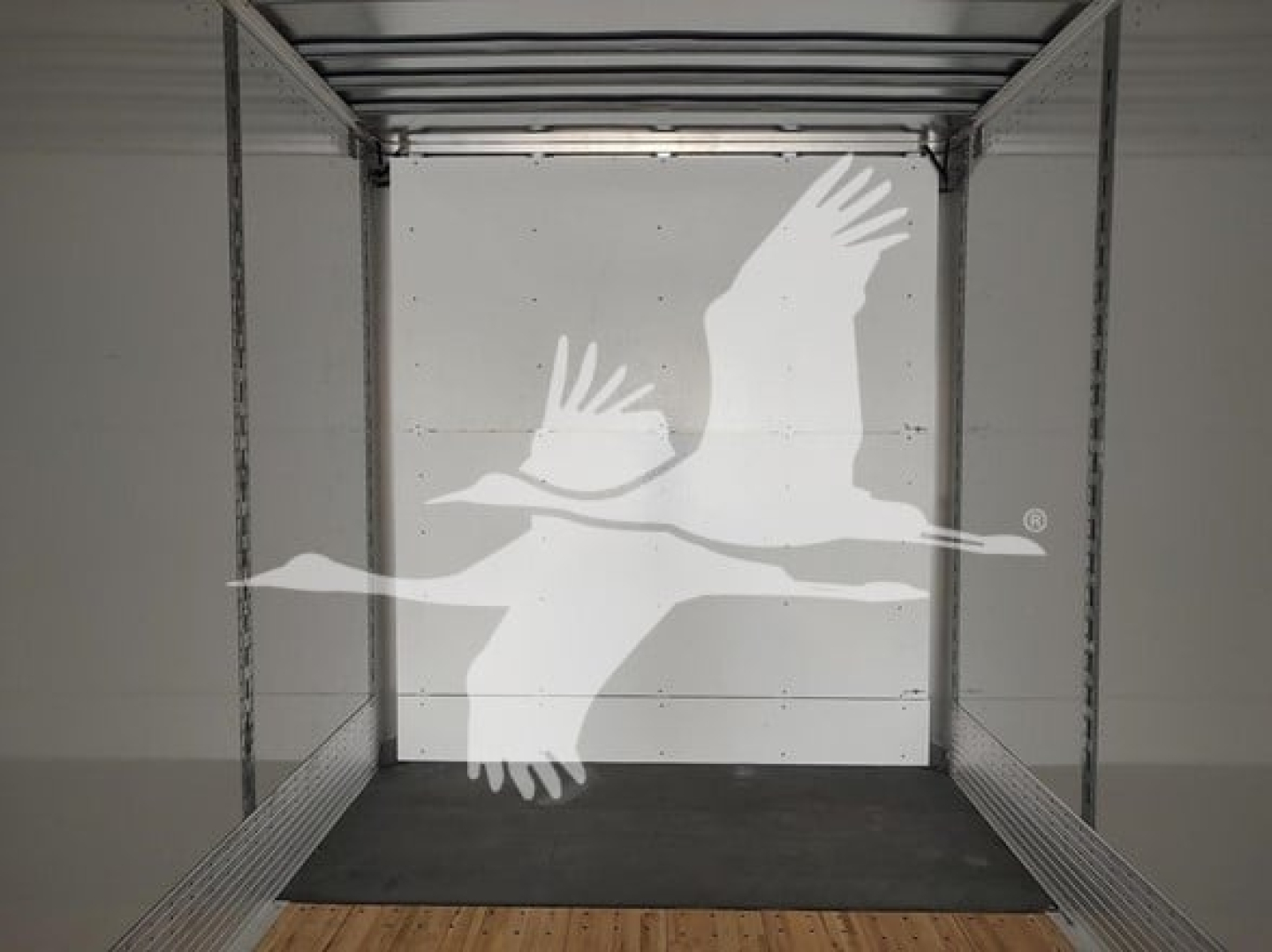 Trailer interior with open rear doors showing loading floor and side rails; watermark of flying geese logo centered.